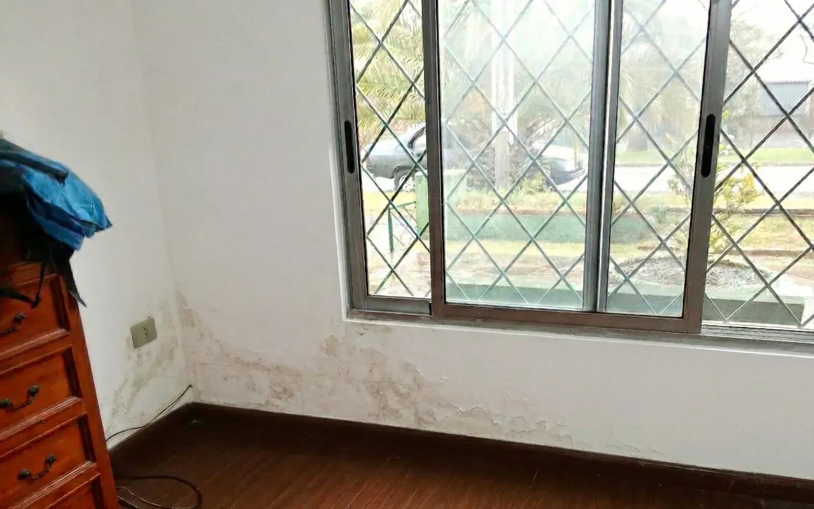 Pared de dormitorio con humedad bajo la ventana antes del tratamiento